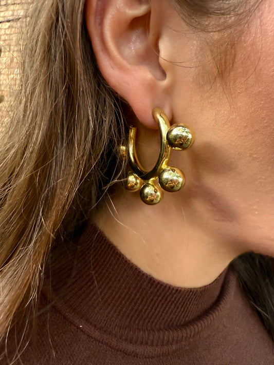 Close-up of a person wearing gold hoop earrings with small spherical accents.