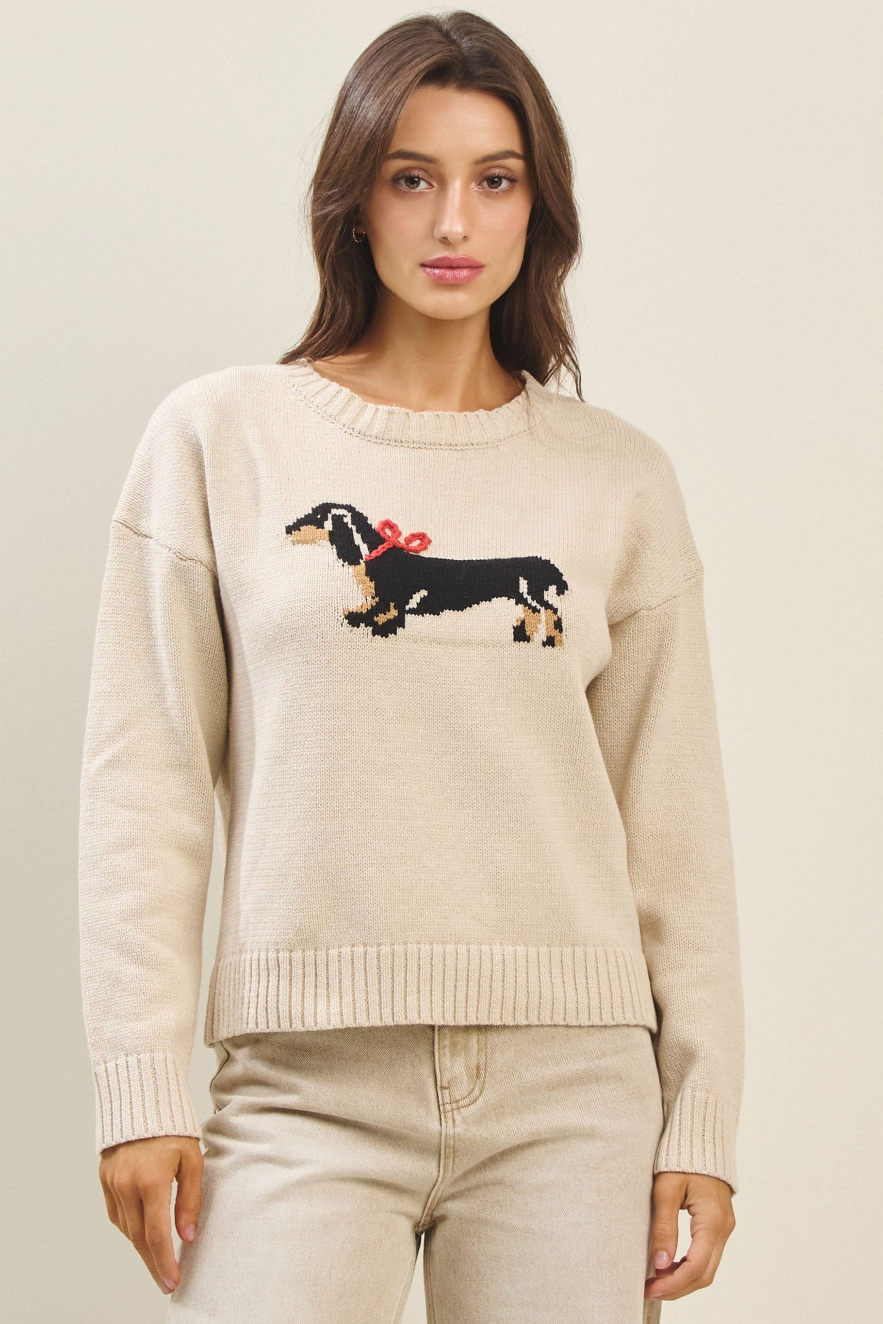Woman wearing a beige sweater with a dachshund design on a plain background