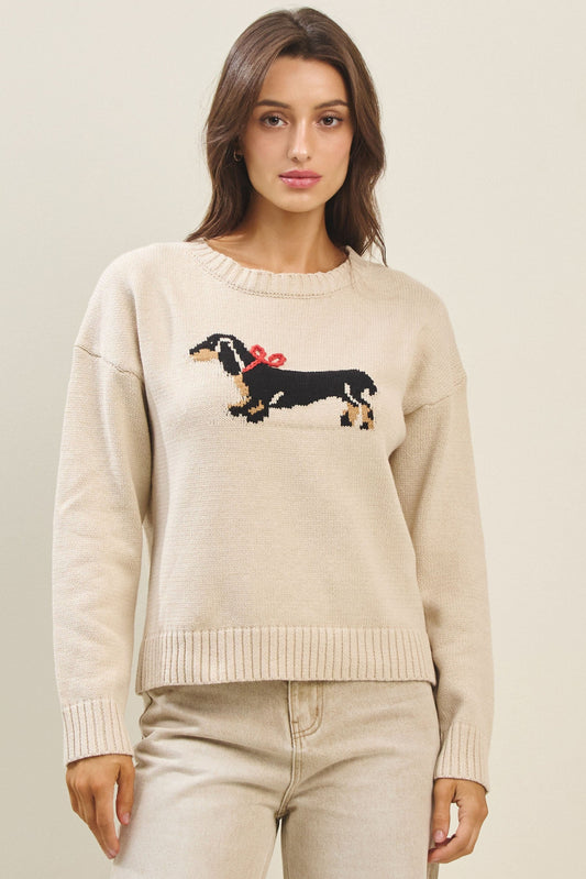 Woman wearing a beige sweater with a dachshund design on a plain background