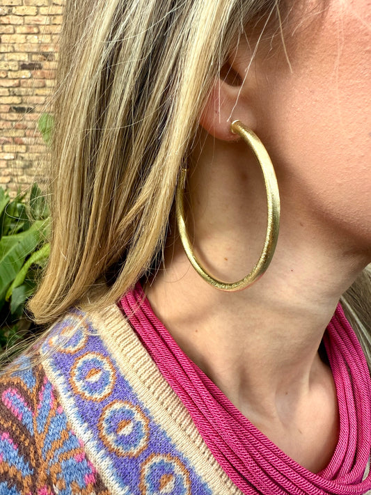 Close-up of a person wearing gold hoop earrings with a colorful garment in the background.