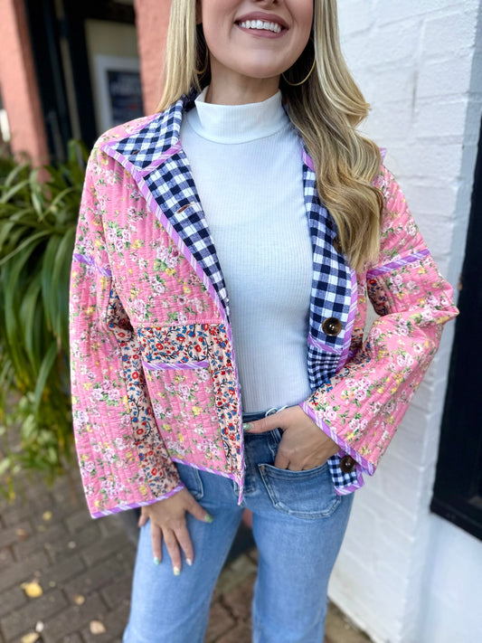 Woman wearing a pink floral and checkered jacket with a white turtleneck and blue jeans.