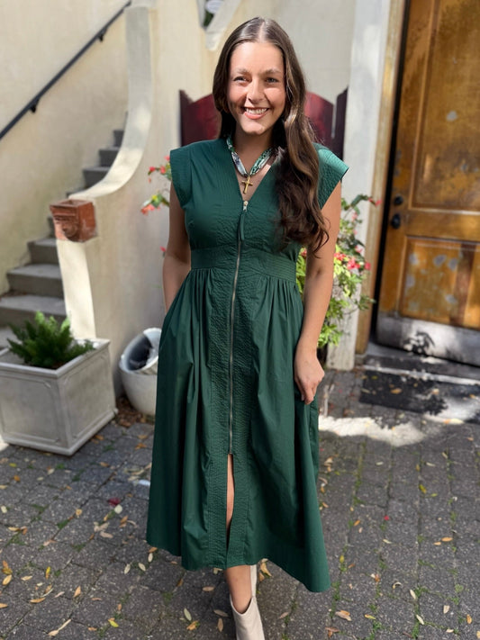 Woman in a green dress standing outdoors on a sidewalk.