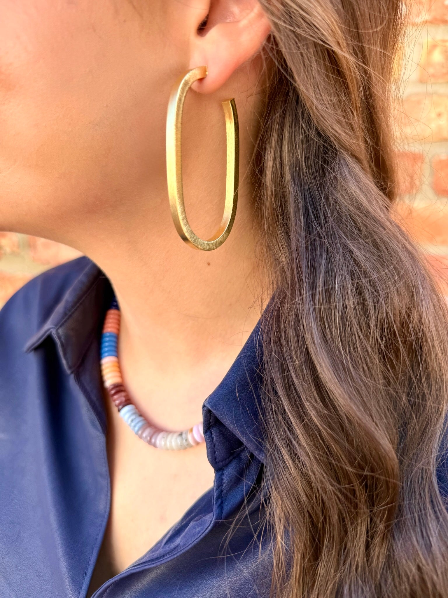 Close-up of a person wearing gold hoop earrings and a blue shirt with a colorful necklace.