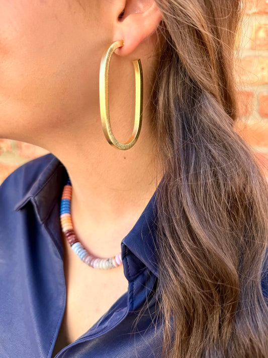 Close-up of a person wearing gold hoop earrings and a blue shirt with a colorful necklace.