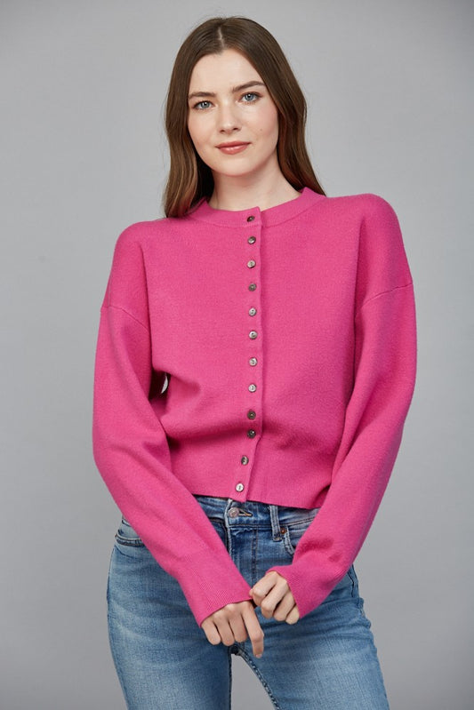 Woman wearing a pink sweater with button details against a gray background