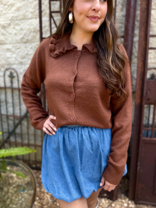 Woman wearing a brown cardigan and blue skirt standing outdoors.