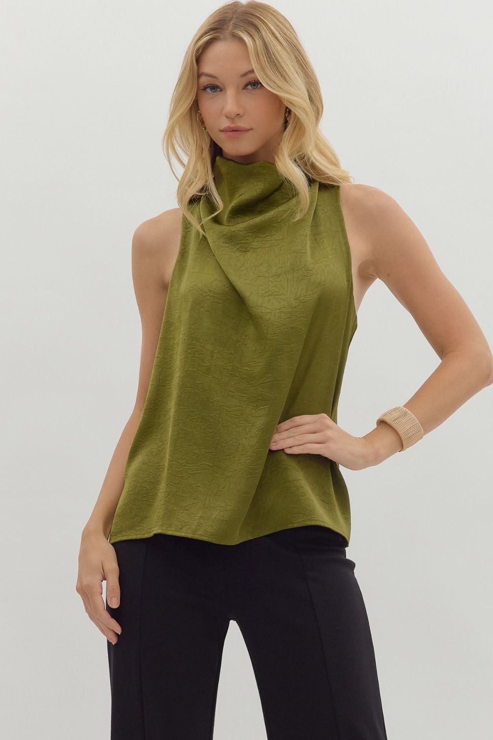 Woman wearing a green sleeveless top with a cowl neck against a plain background