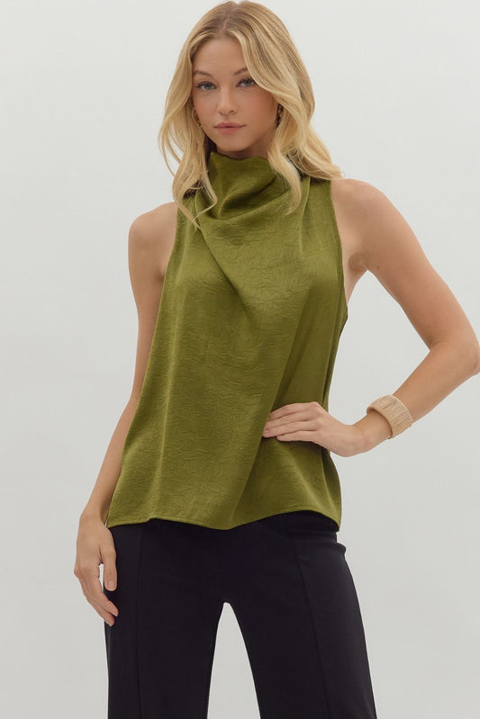 Woman wearing a green sleeveless top with a cowl neck against a plain background