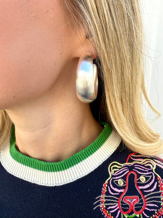Person wearing large silver hoop earrings with a colorful sweater featuring a tiger design.