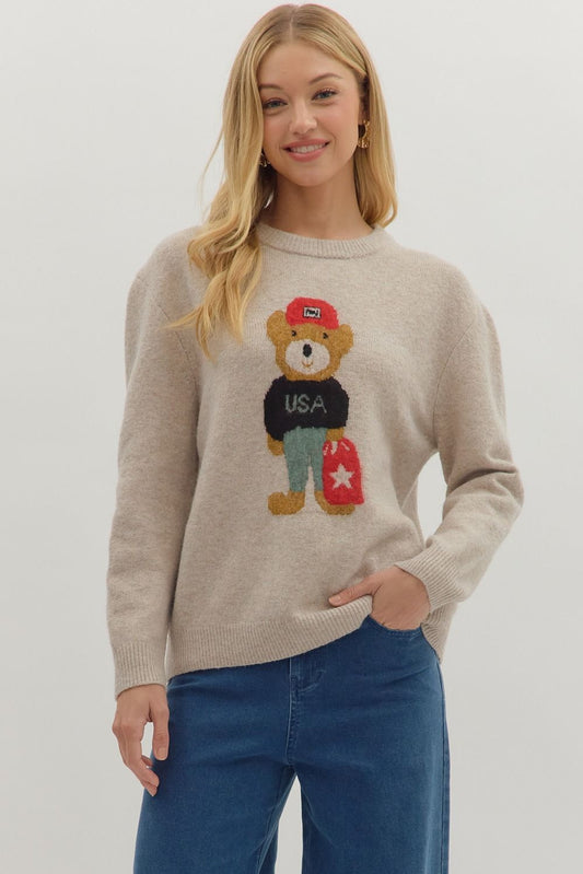 Woman wearing a beige sweater with a teddy bear graphic on a plain background